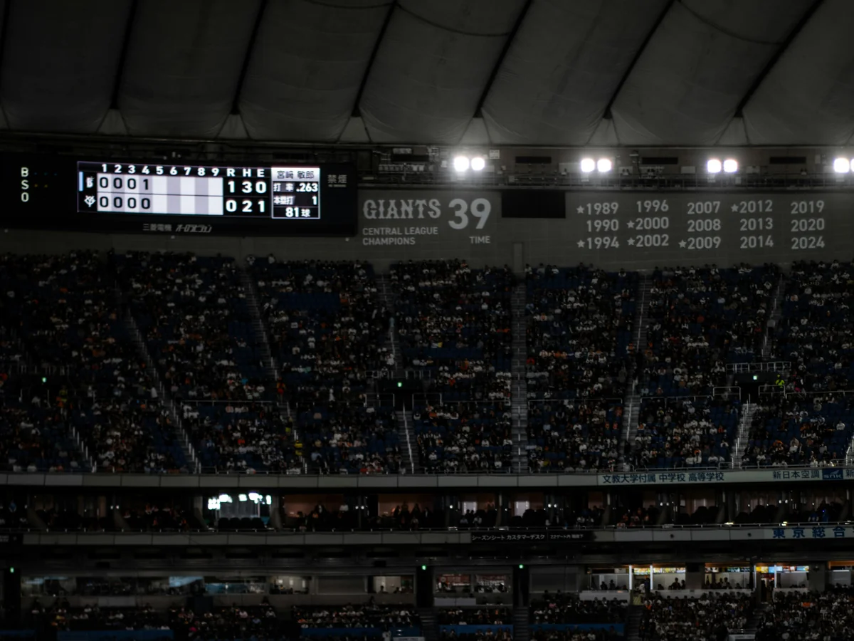 The Tokyo Dome roof structure and the Giants' scoreboard, showing the team's Central League championship years, above the packed stands during a night game